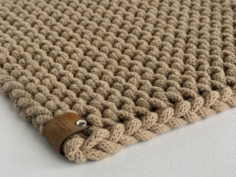 May include: A beige knitted trivet with a brown leather tag that says "Handmade with Love".