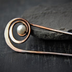 May include: A copper hair stick with a spiral design and a white pearl accent.