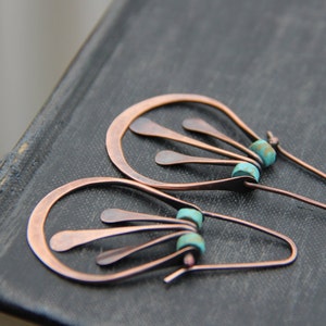 May include: A pair of copper earrings with turquoise beads. The earrings are shaped like a teardrop with a delicate, fan-like design.