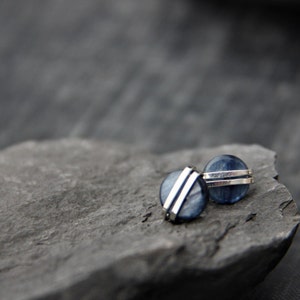 May include: A pair of silver earrings with blue gemstone accents. The earrings are round and have a silver band around the edge.