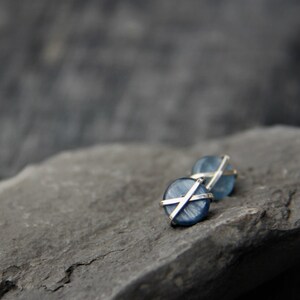 May include: A pair of silver earrings with blue gemstone accents. The gemstones are round and have a criss-cross pattern of silver wire.