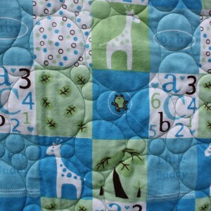 May include: A blue and green baby quilt with a quilted pattern of circles. The quilt features a variety of designs, including giraffes, letters, and numbers. The quilt is made of soft, comfortable fabric and is perfect for a baby's nursery.