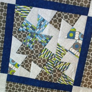 Könnte beinhalten: Ein Quiltblock mit einem geometrischen Muster in Blautönen, Grün, Weiß und Grau. Der Block besteht aus kleineren Quadraten und Dreiecken, und das Muster wiederholt sich über den gesamten Block.