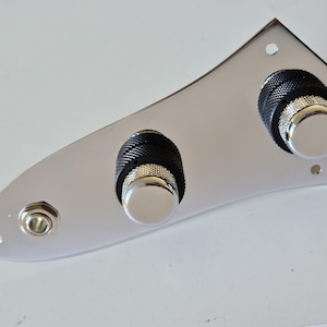 Puede incluir: Una placa de control cromada con tres perillas y un conector. Las perillas tienen un agarre negro texturizado y una tapa plateada. La placa tiene tres orificios para tornillos para el montaje. Componente para guitarra o bajo.