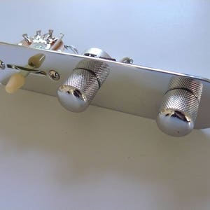 Op de afbeelding: Een verchroomde gitaarbedieningsplaat met twee getextureerde knoppen, een schakelaar en diverse elektronische componenten. De ovale plaat heeft montagegaten en zichtbare bedrading.