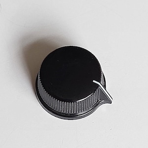 以下が含まれることがあります： 黒いプラスチック製のノブで、縁に溝があり、白いインジケーターラインが付いています。ノブは円形で、設定を調整するためのもののようです。デザインはシンプルで機能的です。