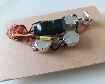 May include: Guitar electronics assembly on a light brown wooden base. The components include potentiometers, a switch, capacitors, and wiring. The assembly is designed for a guitar and is ready for installation.