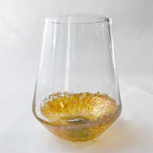 May include: A clear glass wine glass with a speckled gold and white design around the bottom.
