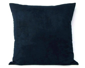 Puede incluir: Un cojín cuadrado de terciopelo azul marino. El cojín tiene una textura suave y afelpada y un diseño de color liso. El cojín es un elemento decorativo para una cama o un sofá.