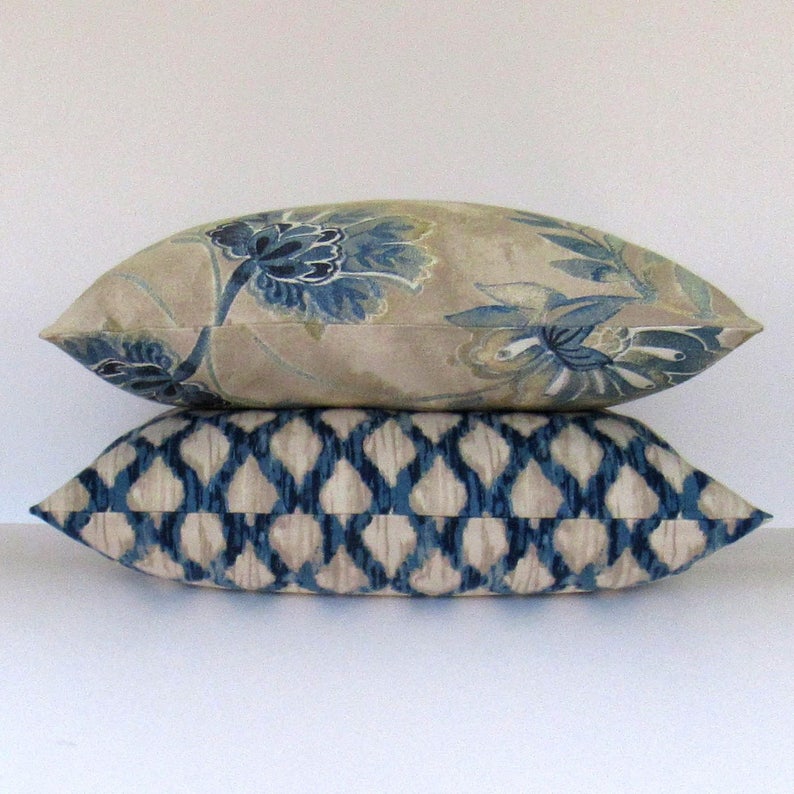 K&ouml;nnte beinhalten: Zwei dekorative Kissen, eines mit einem Blumenmuster in Blau- und Beiget&ouml;nen, das andere mit einem geometrischen Muster in Blau- und Beiget&ouml;nen.