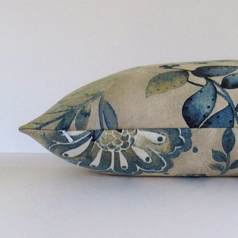 K&ouml;nnte beinhalten: Ein beigefarbenes Kissen mit einem blauen und gr&uuml;nen Blumendesign. Das Kissen hat einen Rei&szlig;verschluss.