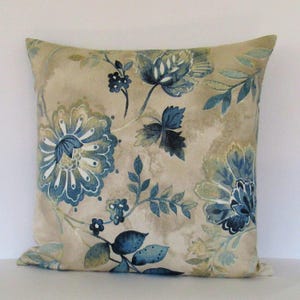 K&ouml;nnte beinhalten: Beigefarbener Kissenbezug mit einem blauen und gr&uuml;nen Blumenmuster. Das Kissen zeigt eine gro&szlig;e blaue Blume mit wei&szlig;en Akzenten in der Mitte.