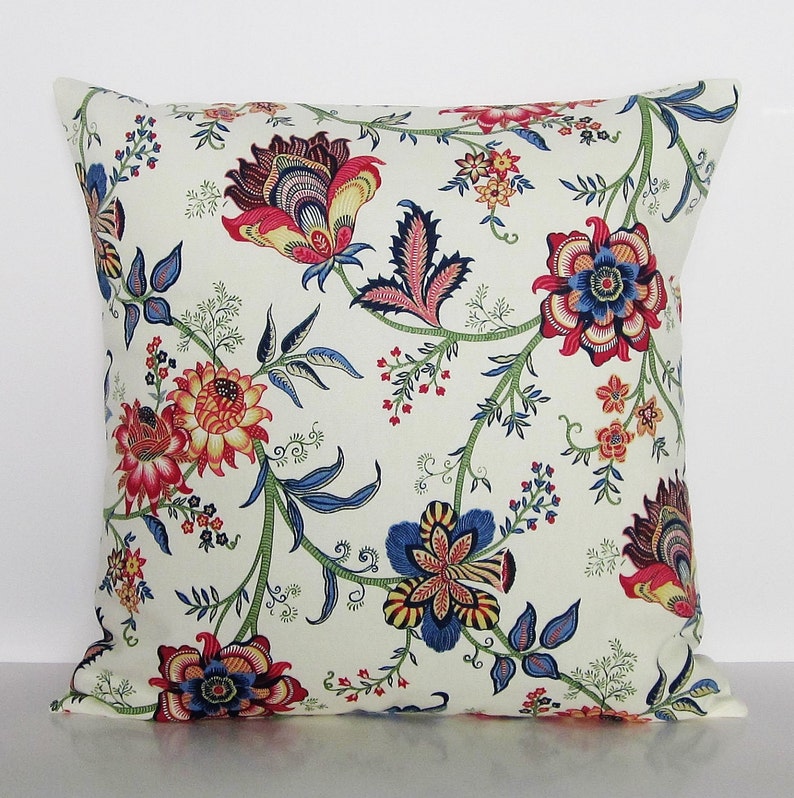 Puede incluir: Una almohada blanca con un patr&oacute;n floral en tonos rojos, azules y verdes. Las flores son estilizadas y tienen un aspecto vintage.