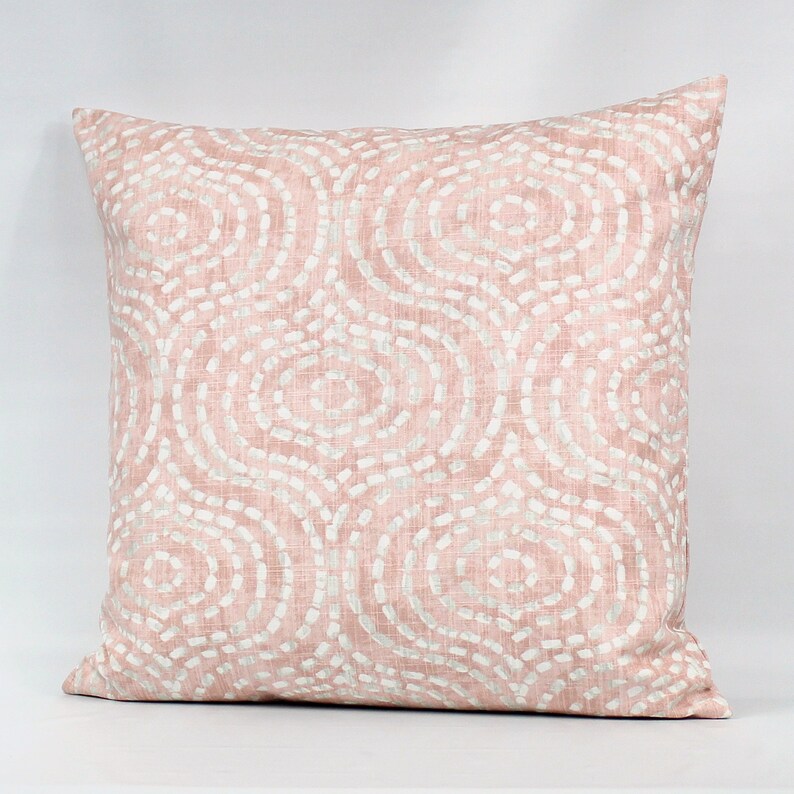 Puede incluir: Una almohada rosa con un patr&oacute;n de remolino blanco. La almohada est&aacute; hecha de una tela suave y texturizada.