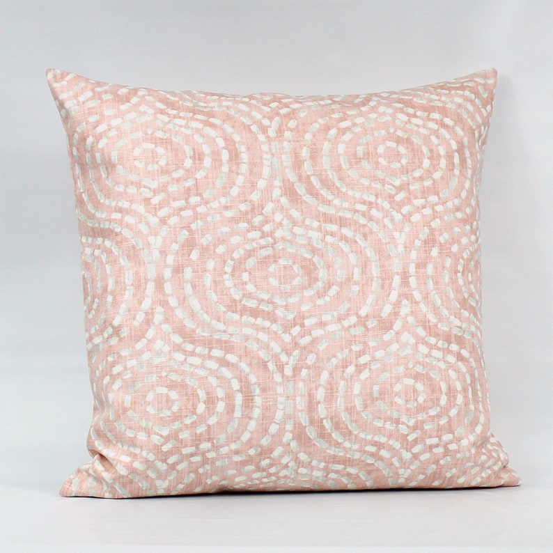 Puede incluir: Una almohada rosa con un patr&oacute;n geom&eacute;trico blanco de c&iacute;rculos. La almohada est&aacute; hecha de una tela suave y texturizada.
