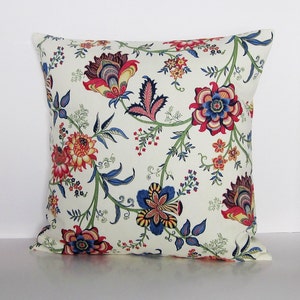 Puede incluir: Una almohada blanca con un patr&oacute;n floral en tonos rojos, azules y amarillos. Las flores son estilizadas y tienen un aspecto vintage.