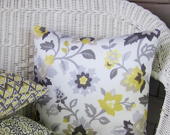 Puede incluir: Una silla de mimbre blanca con dos cojines. Un cojín tiene un estampado floral gris y amarillo, y el otro tiene un estampado geométrico en tonos grises y amarillos.