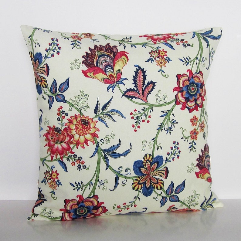 Puede incluir: Una almohada blanca con un patr&oacute;n floral en tonos rojos, azules y verdes. Las flores son estilizadas y tienen un aspecto vintage.
