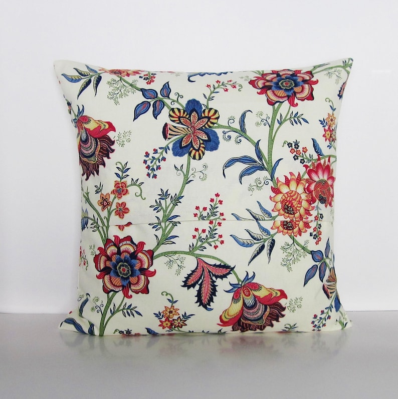 Puede incluir: Una almohada blanca con un patr&oacute;n floral en tonos rojos, azules y amarillos. Las flores son estilizadas y tienen un aspecto vintage.