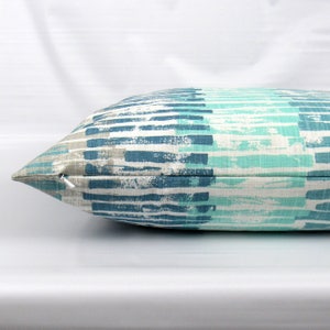 Puede incluir: Una almohada rectangular larga con cierre de cremallera. La funda de la almohada presenta un patr&oacute;n geom&eacute;trico de rayas azules, verde azulado y blancas.