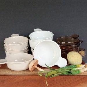 Pode incluir: Uma cole&ccedil;&atilde;o de tigelas de sopa de cer&acirc;mica creme, brancas e castanhas. Cada tigela tem uma al&ccedil;a. As tigelas est&atilde;o dispostas numa t&aacute;bua de madeira com vegetais decorativos, incluindo cebolinho e um cogumelo.