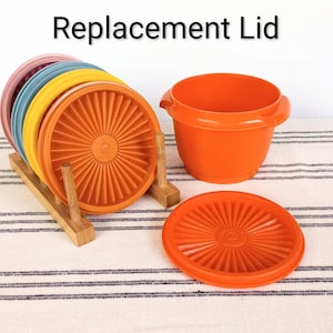 May include: An assortment of colorful replacement lids in pink, blue, yellow, and orange, displayed on a wooden rack. An orange bowl and lid are also present. The text "Replacement Lid" is at the top.