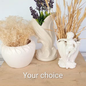 May include: Three white ceramic vessels, including a rounded bowl, a tall flared vase, and a cherub-adorned planter, filled with dried beige grasses and purple flowers. The text "Your choice" is centered at the bottom of the image.