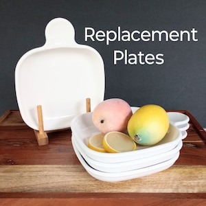 May include: White ceramic serving plates with a handle and a stack of square plates. The text "Replacement Plates" is displayed. Decorative fruit, including a peach, lemon, and lemon slices, are arranged on the plates.