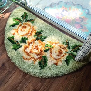 May include: A semi-circular shag rug featuring a light green background with a prominent floral pattern of three large, textured roses in shades of cream, yellow, and orange, accented by deep green leaves and stems throughout the design.