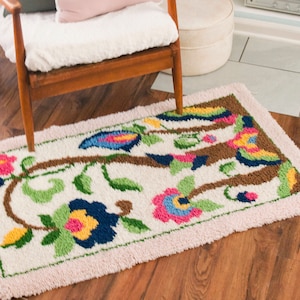 May include: A white rug with a pink border features a colorful floral design with brown branches, blue, pink, yellow, and green flowers.