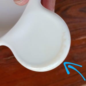 Pode incluir: Uma caneca de cer&acirc;mica branca com uma al&ccedil;a curva. A caneca tem um acabamento liso e brilhante e uma base arredondada. O interior da caneca tamb&eacute;m &eacute; branco. A caneca est&aacute; limpa e parece n&atilde;o utilizada.