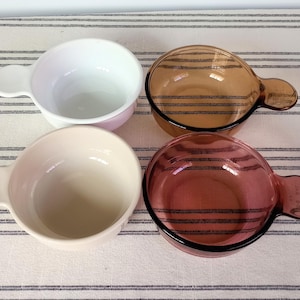 Pode incluir: Quatro tigelas de vidro com al&ccedil;as, em branco, rosa claro, &acirc;mbar e vermelho-p&uacute;rpura. As tigelas s&atilde;o redondas com uma al&ccedil;a de um lado. As tigelas &acirc;mbar e vermelho-p&uacute;rpura t&ecirc;m listras pretas. As tigelas est&atilde;o em uma superf&iacute;cie listrada branca e cinza.