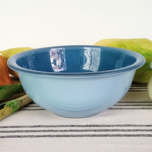 May include: A light blue ceramic mixing bowl with a white interior. The bowl is sitting on a white and black striped tablecloth.