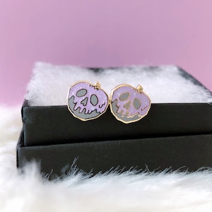 May include: A pair of purple and gold glitter skull earrings shaped like a poisoned apple.