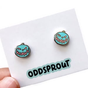 May include: A pair of teal blue enamel pumpkin earrings with pink and white details. The earrings are on a white card with the text "ODDSPROUT" in black.