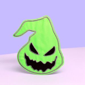 May include: Green felt patch with a black stitched outline of a ghost with a wide grin and two eyes. The ghost is wearing a pointy hat.