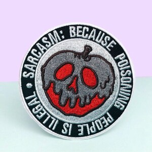 Puede incluir: Parche bordado redondo con un dise&ntilde;o gris, rojo y negro. El parche presenta una manzana con forma de calavera con el texto "Sarcasm: Because People is Illegal Poisoning."