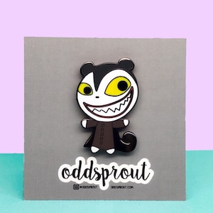 May include: A black and white enamel pin featuring a cartoon character with a large, toothy grin and yellow eyes. The character is wearing a brown coat and has a small tail. The pin is on a gray background with a white sticker that says "oddsprout" and includes the social media handle "@oddsprout" and website "oddsprout.com".