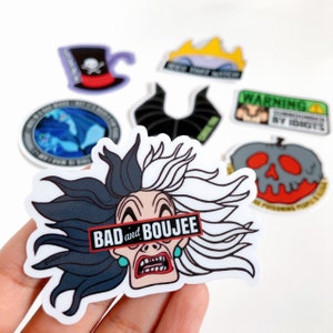 May include: A sticker featuring a cartoon image of Cruella De Vil from Disney's 101 Dalmatians. The sticker has a black and white design with a red and white banner across the middle that reads "Bad and Boujee".