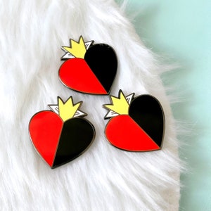 May include: Three enamel pins shaped like hearts, each with a gold crown on top. The hearts are split in half, one side red and the other black.