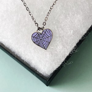 May include: A silver chain necklace with a purple heart pendant featuring a spiderweb design.