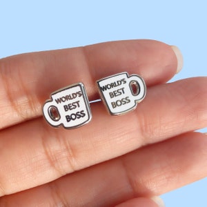 May include: A pair of silver earrings shaped like coffee mugs with the text "World's Best Boss" on them.