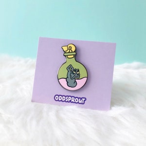 May include: Green glass bottle with a yellow stopper and a pink liquid inside. A gray creature with two eyes is inside the bottle. The bottle is on a purple card with the text "ODDSPROUT".