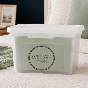 May include: A clear plastic storage bin with a lid, featuring a circular black decal on the front that displays the name WILLIAM ETHAN in a clean, sans-serif font. The container is rectangular with a secure snap-on lid and smooth edges.