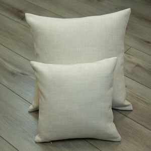Two beige throw pillows are placed on a wooden floor.
