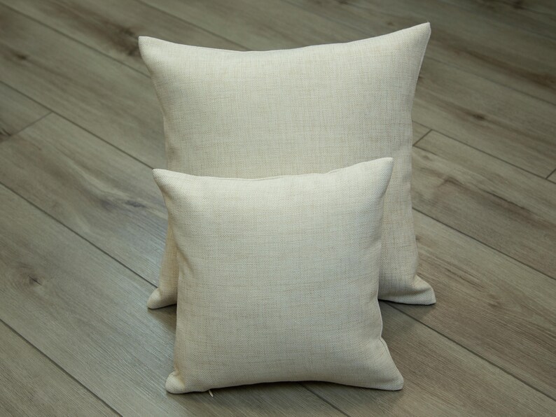 Two beige throw pillows are placed on a wooden floor.