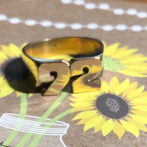 May include: A gold-colored ring with the number "92" embossed on the top. The ring is sitting on a brown surface with a sunflower pattern.