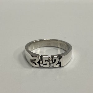 May include: A silver ring with the numbers 3-5-2 engraved on the band.