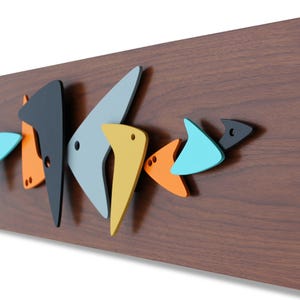 May include: A wooden wall art piece featuring a series of colorful, abstract fish shapes in various colors, including black, gray, orange, yellow, and blue. The fish are mounted on a dark brown wooden background.