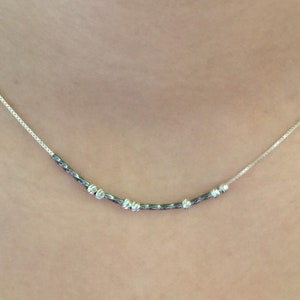 May include: A silver necklace with a delicate chain and a row of small, silver beads. The beads are spaced evenly along the chain and create a simple, elegant look.